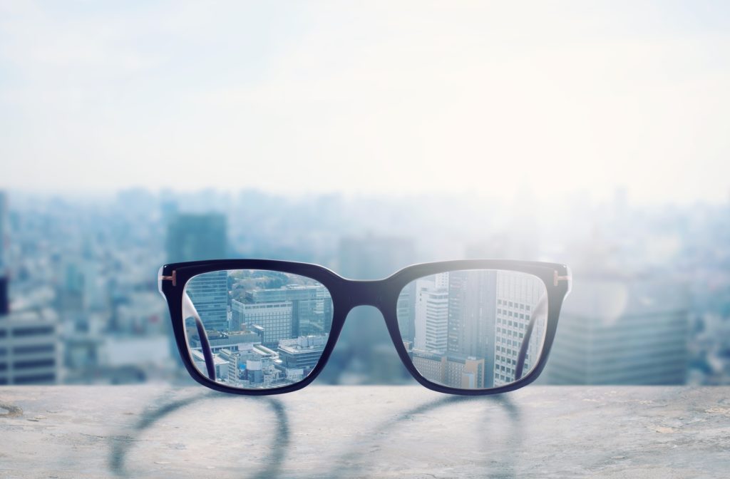 A pair of glasses on a ledge infront of a city landscape, sharpening the view through the lenses with the rest of the city view being blurry