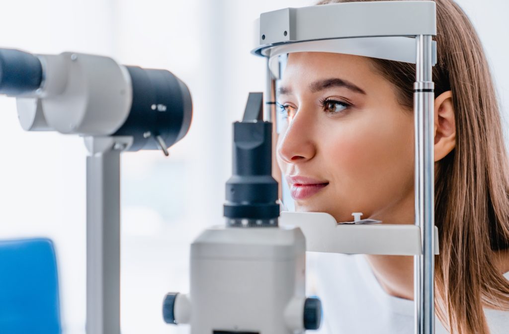 A woman at her optometrist getting a contact lens exam, her chin resting on a slit lamp