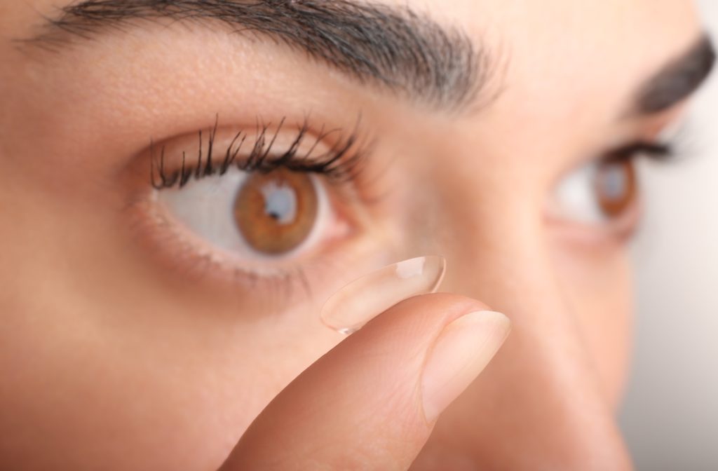 A close up of a woman holding her finger up to her eye with a contact lens resting on the tip ready to place it on her eye
