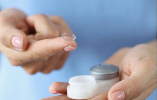 A person holding a contact lens on the tip of their finger as they hold the contact lens case in the other hand