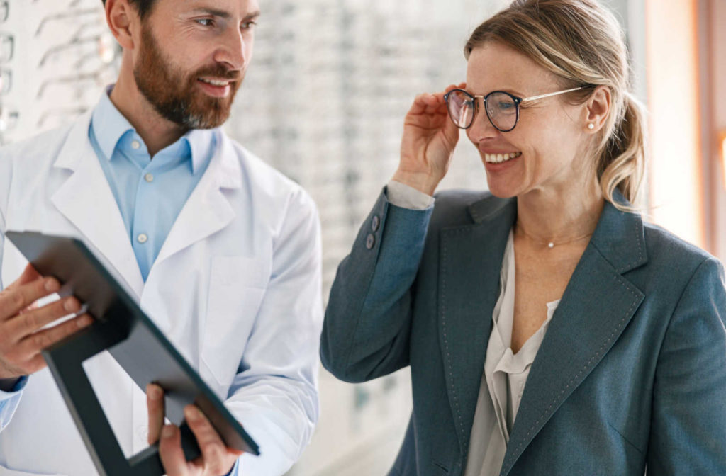 An optician holding a mirror to show the patient they style of glasses they chose