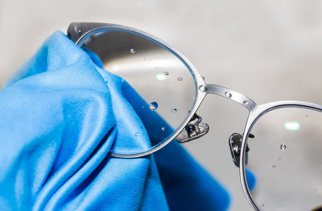 A close up of a pair of glasses getting cleaned with the proper glasses cleaning solution and cloth.
