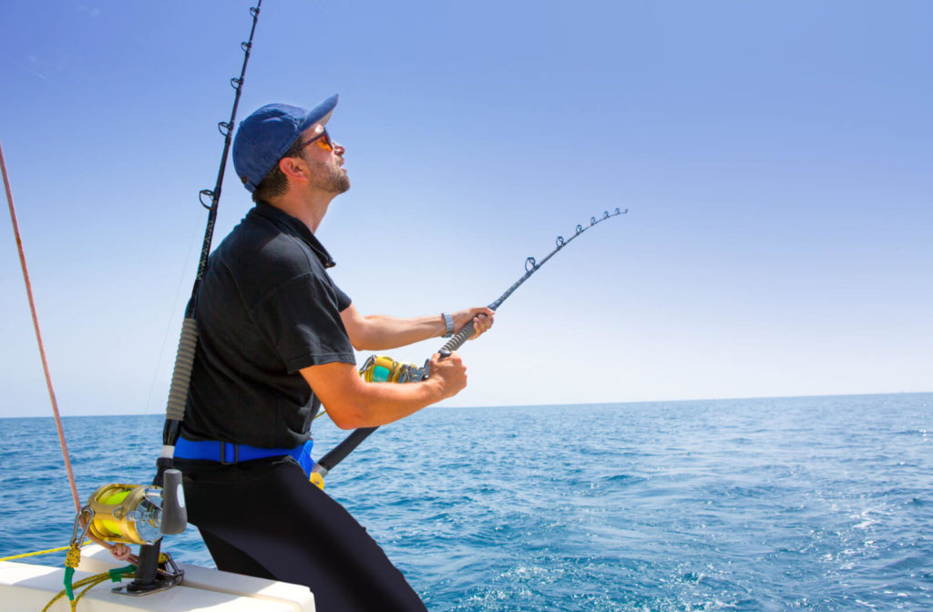 A male sport fishing enthusiast is wearing polarized sunglasses in hot sunny weather while reeling his fishing line.