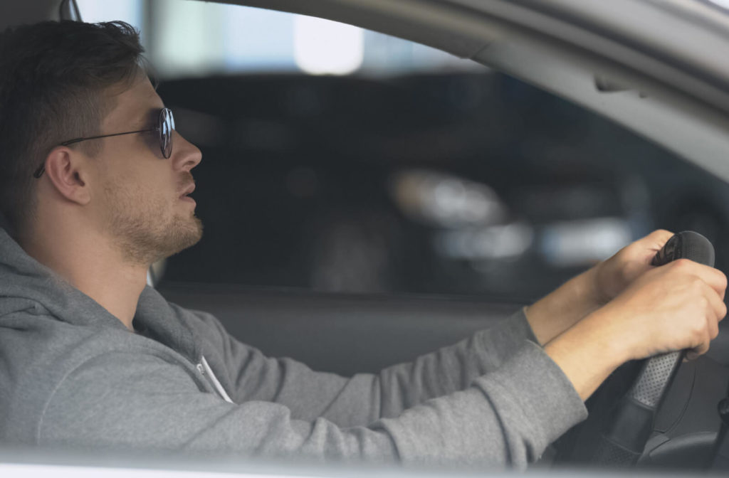 A male driver is wearing polarized sunglasses to reduce the glare from the road and other cars. This can make it easier to see the road and can make it safer to drive in bright conditions.