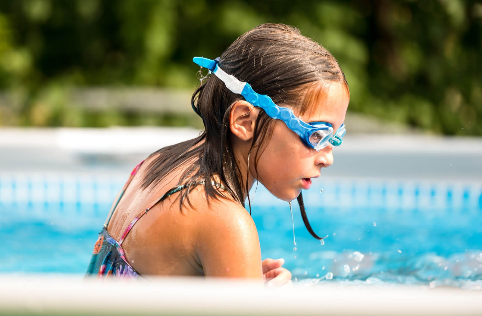 A young girl is wearing swimming goggles while having fun in an outdoor pool.