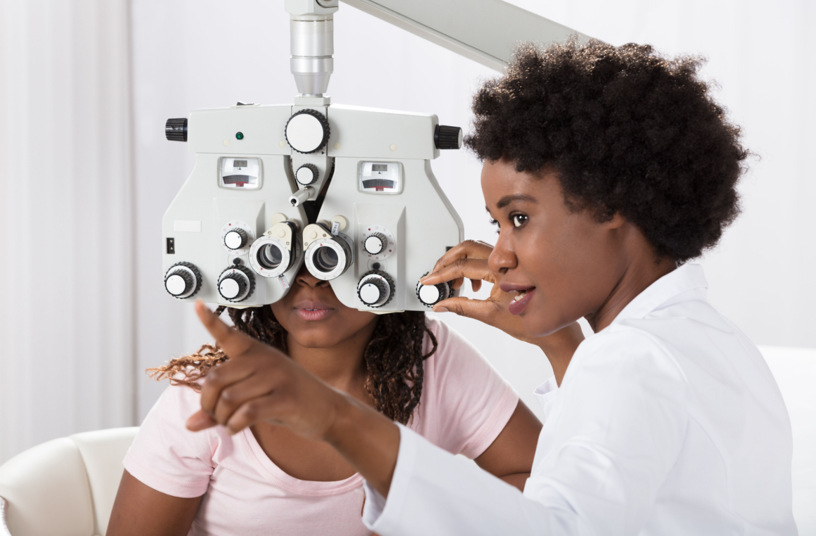 An optometrist conducting an eye exam on her patient using a phoropter.
