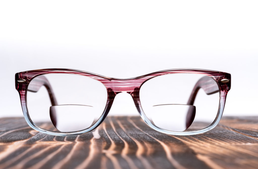 A pair of bifocal glasses sitting on a wood table top.