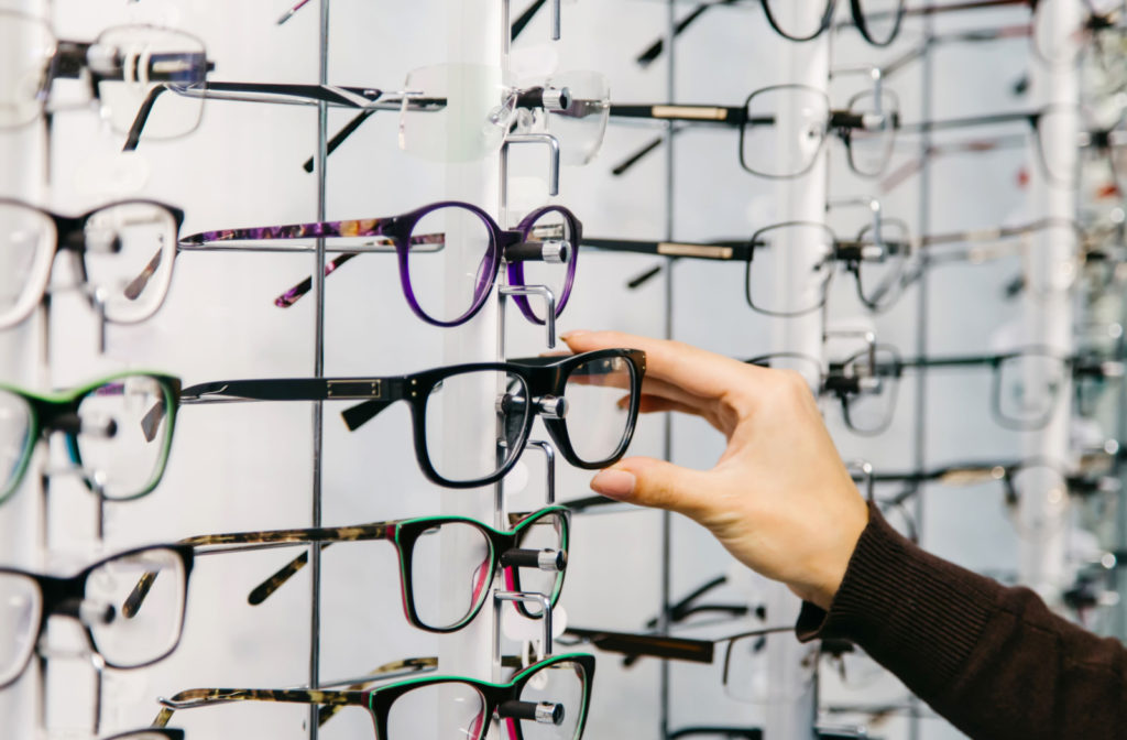 A hand reaching out to grab a pair of eyeglasses from a wall of frames at their local eye clinic.