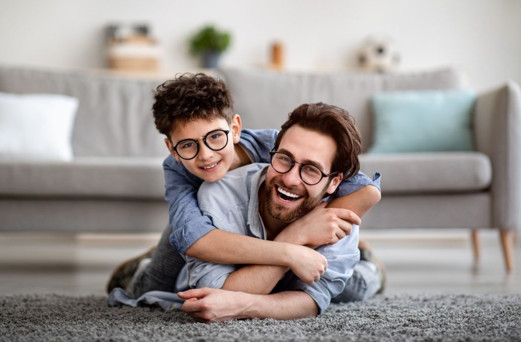 A man and his son wearing glasses and laying on the floor laughing.