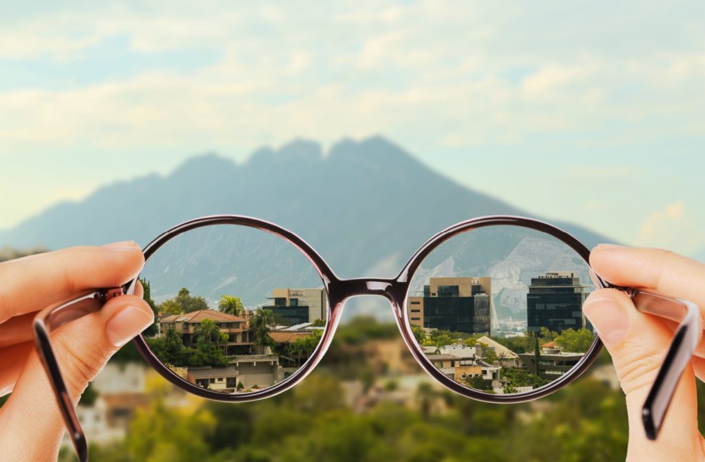 A person is holding their glasses to show what myopia vision looks like, clear through the glasses and a blurry background.