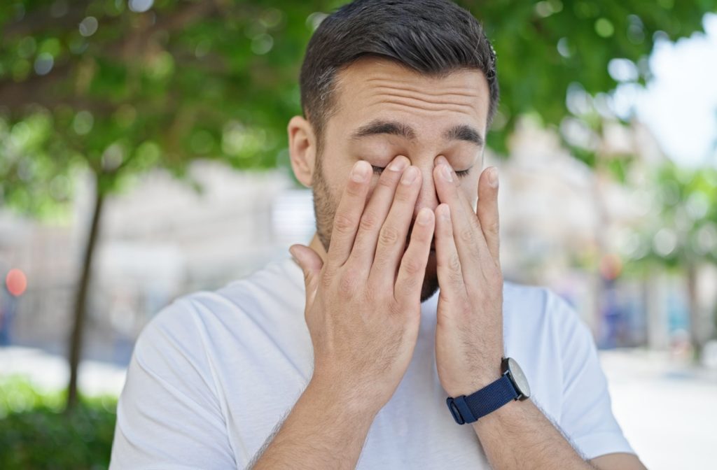 A man outdoors rubbing his eyes to find relief.