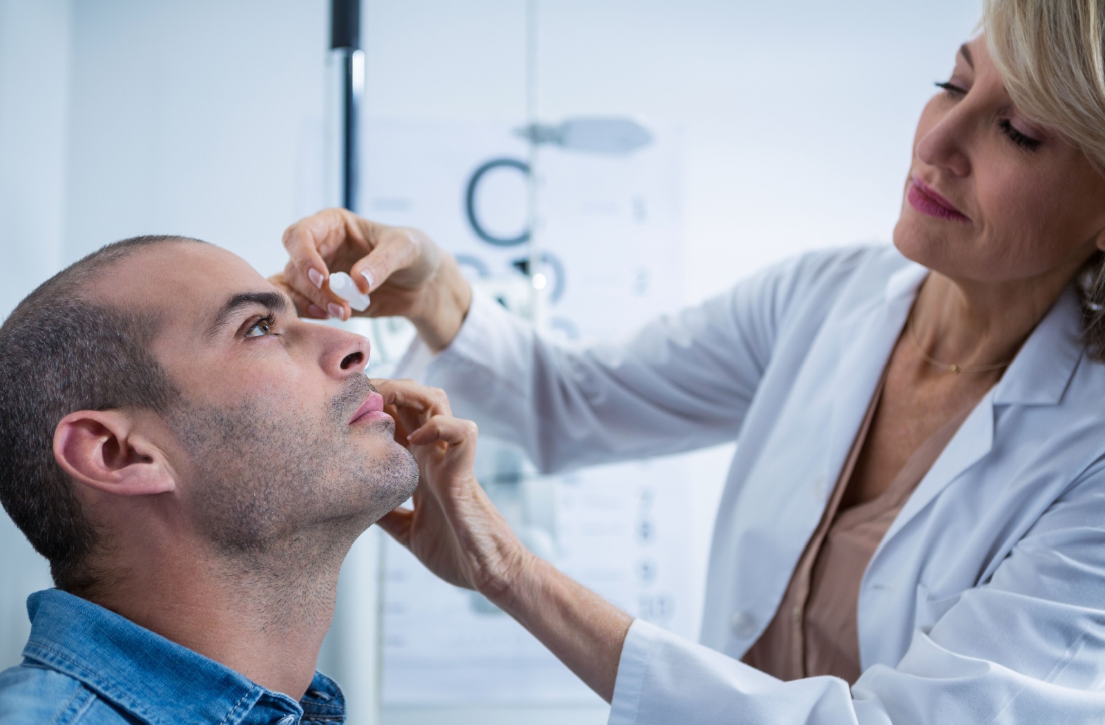 Eye doctor puts medicated eye drops in a man's eyes.