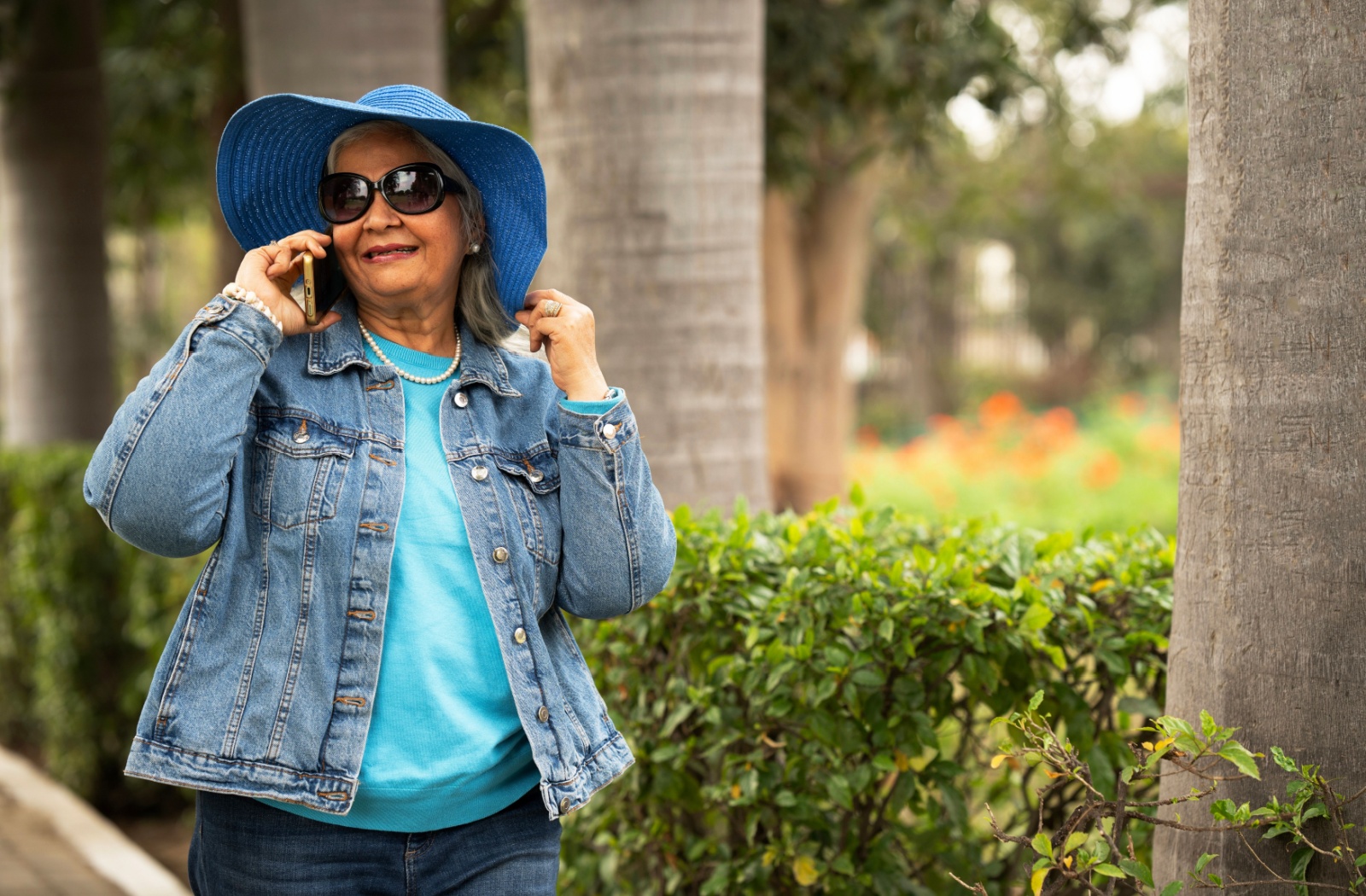 An older woman in a bright blue hat wears sunglasses outside while talking on the phone to protect her eyesight