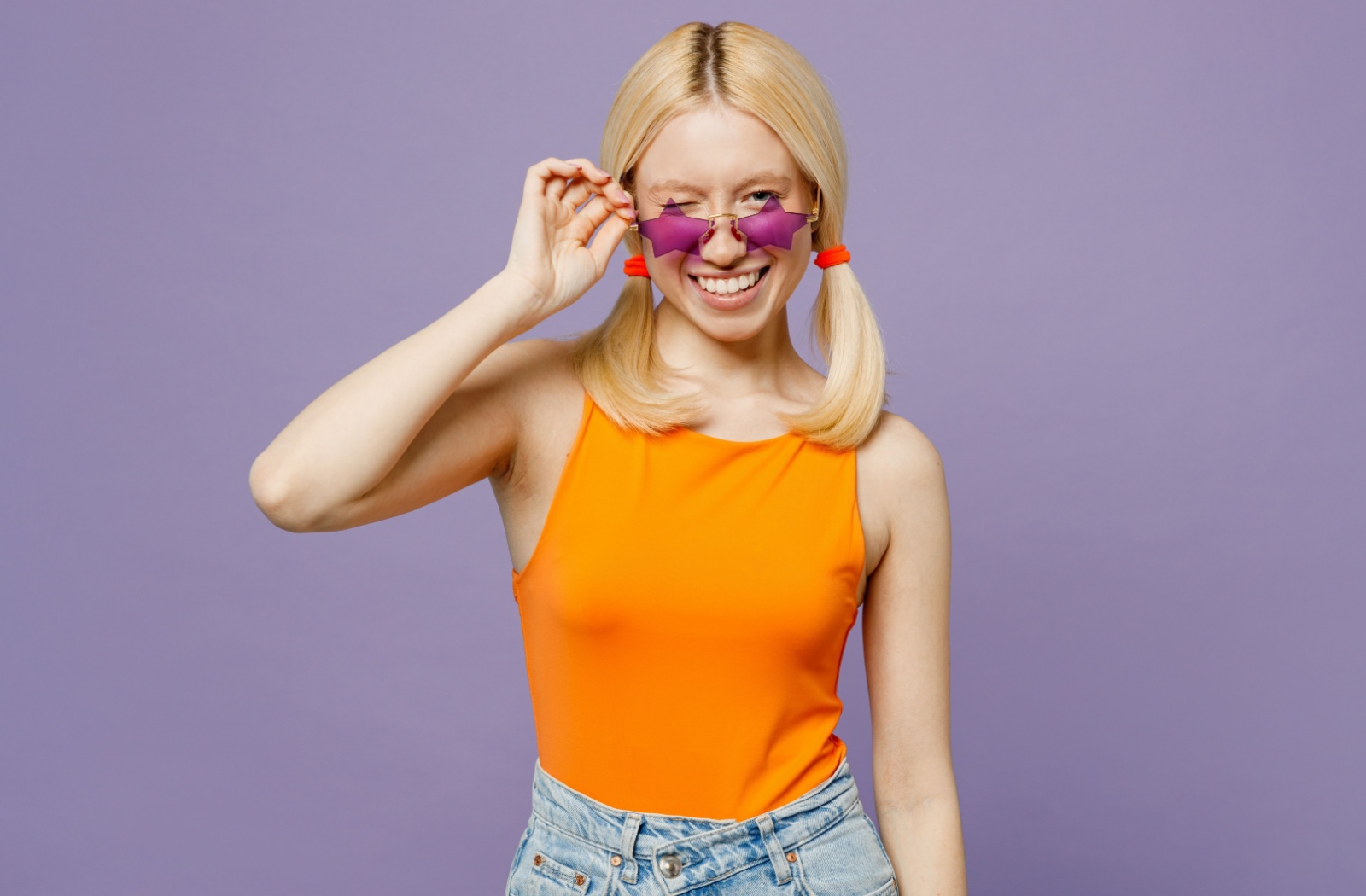 A young adult winks behind a pair of purple-star-shaped sunglasses against a purple background.