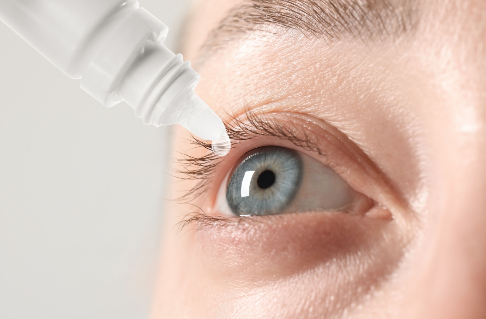 A close-up image of a person applying eye drops to their eye.
