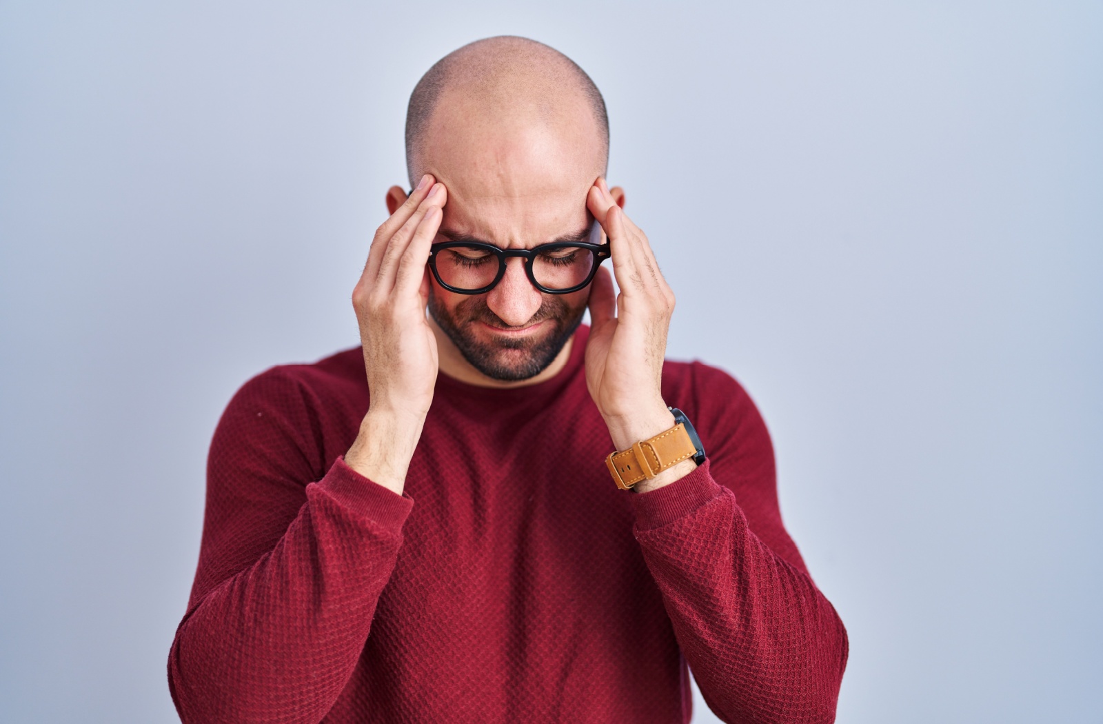 A young man grasps at his temples while experiencing a headache due to his new glasses.
