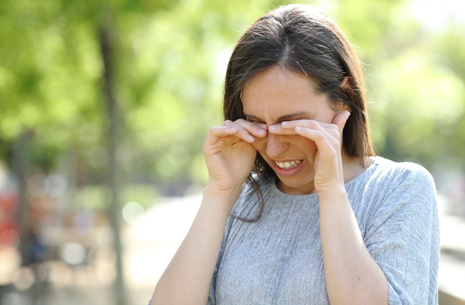 A person outdoors winces and protects their eyes from pollen.