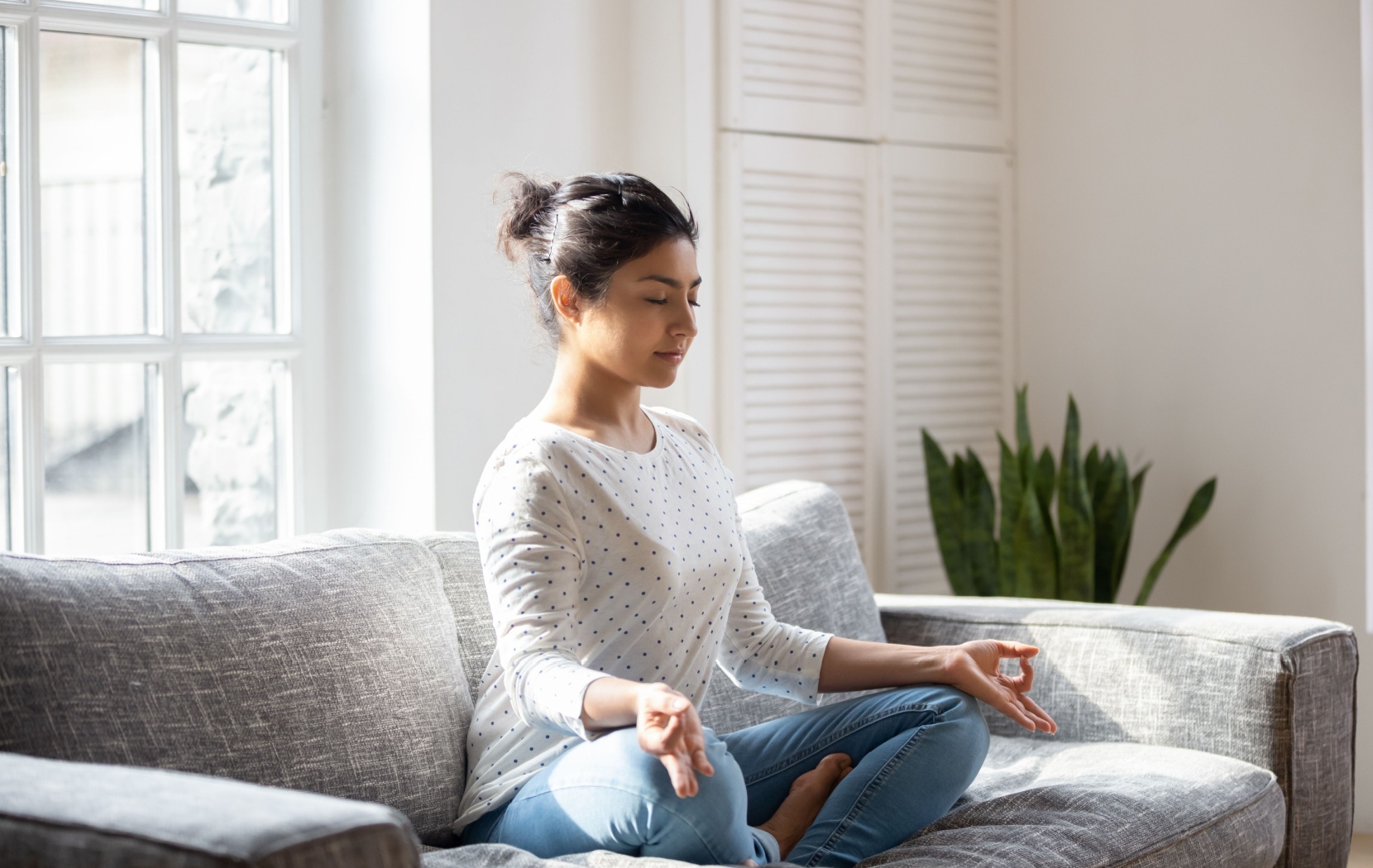 A person sits cross-legged on their couch while meditating to reduce stress and improve their health.
A person sits cross-legged on their couch while meditating to reduce stress and improve their health.