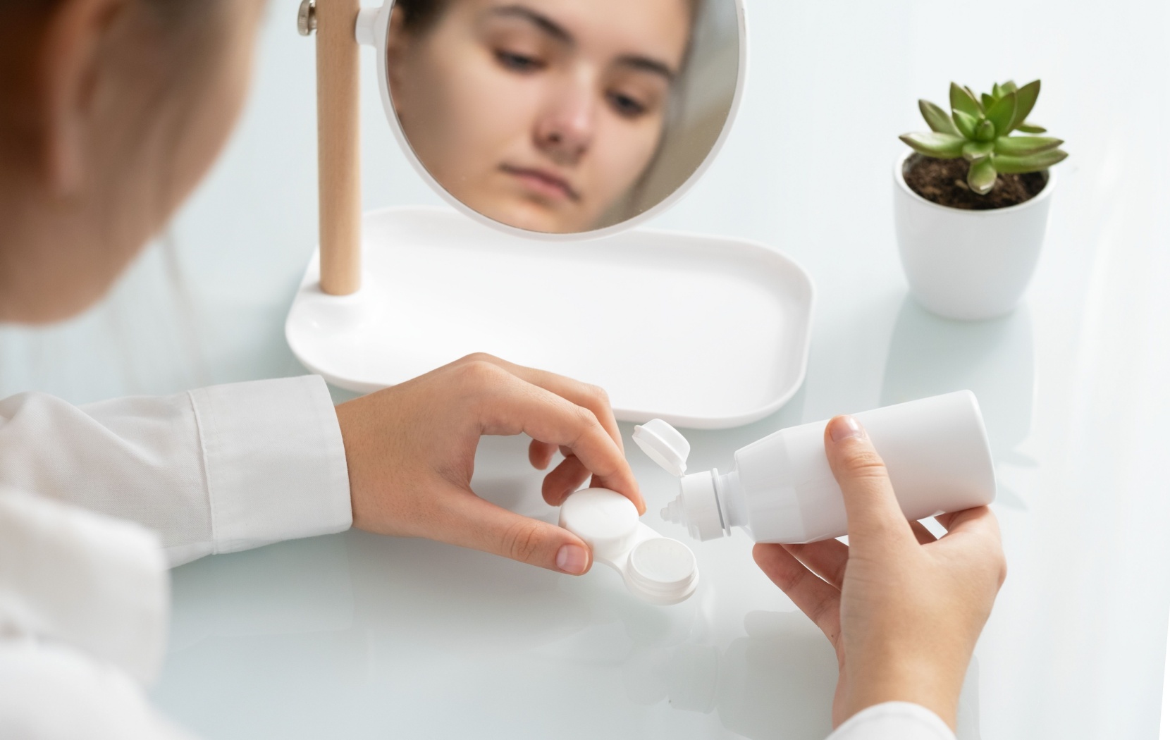 A young adult squeezes cleaning solution into their contact lens case from a new bottle to avoid irritating their eyes.