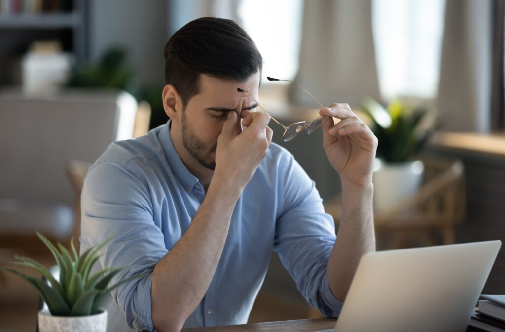 Man with dizziness removes his glasses as he tries to work on his laptop.