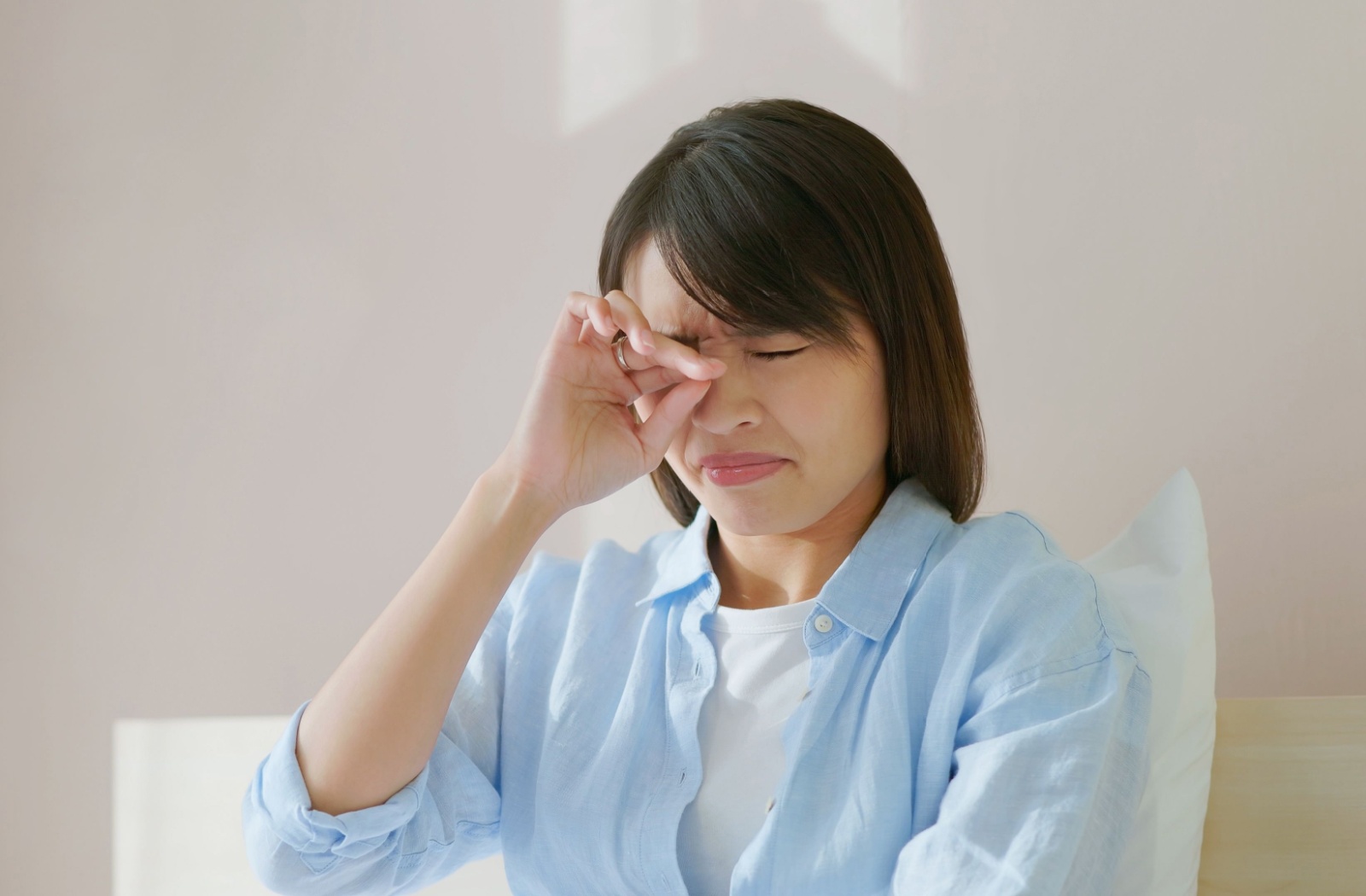 Sick woman sits in bed and rubs her sore eye.