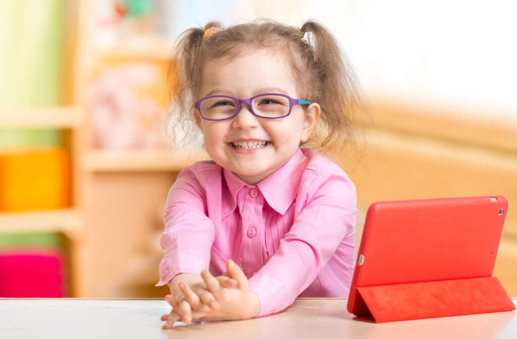 Young smiling girl wearing glasses while working at a tablet.